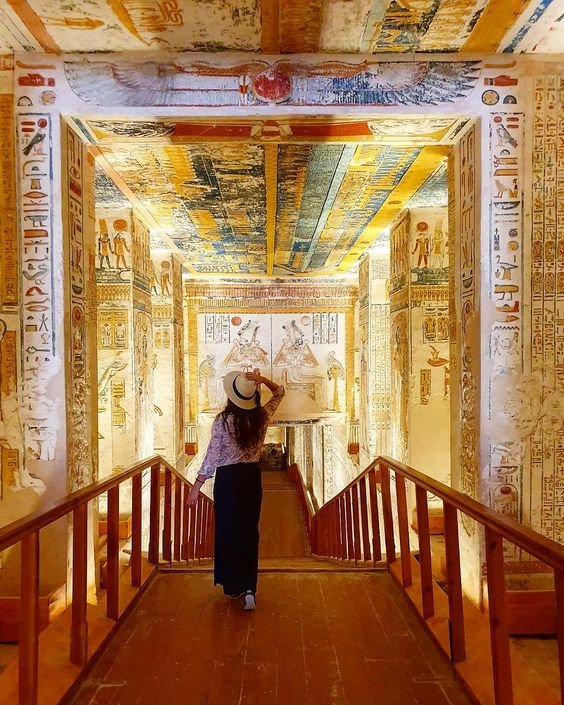 A person inside an ancient Egyptian tomb with hieroglyphics and paintings on the walls and ceiling.