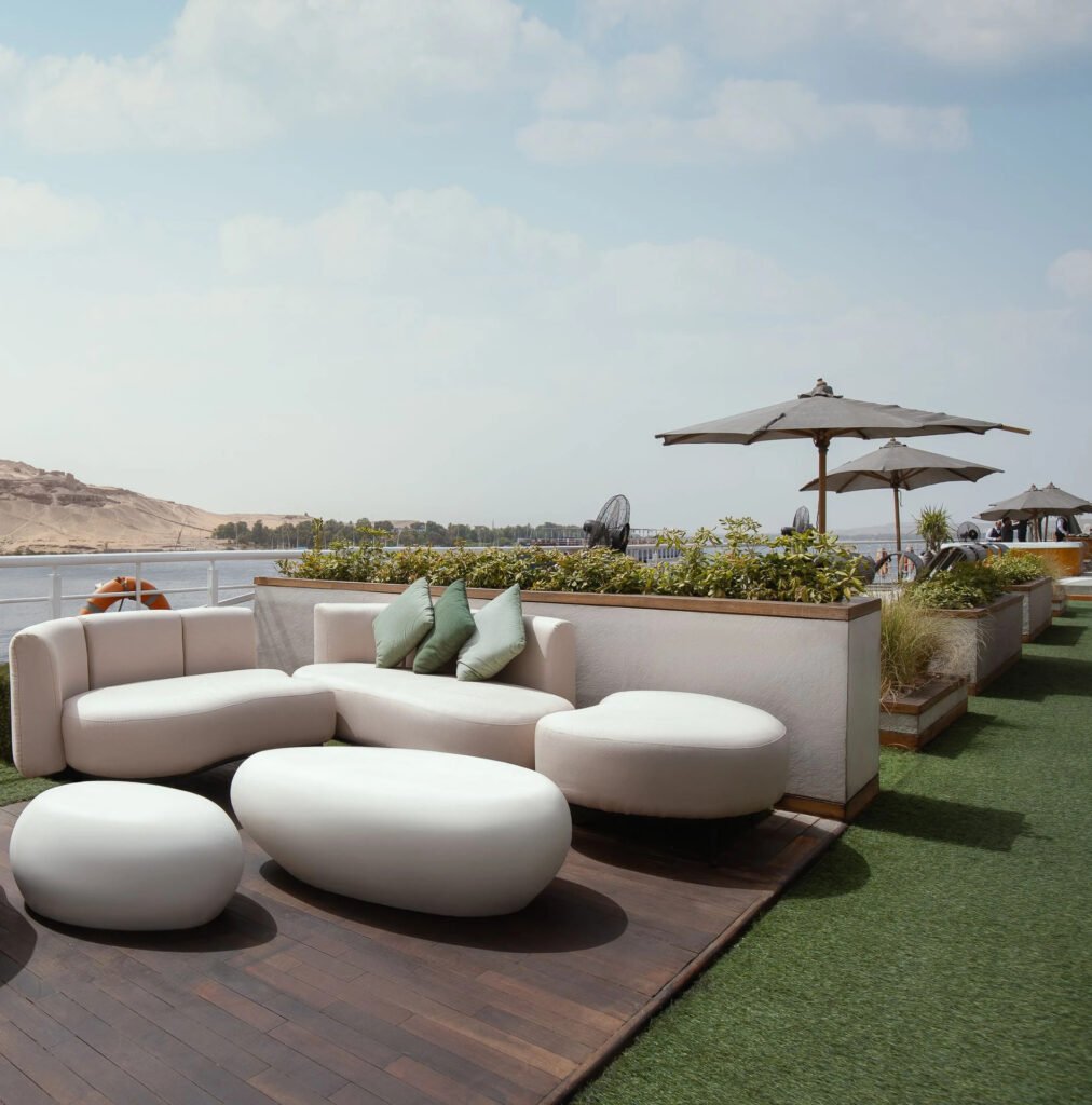 Riverside rooftop lounge with modern white furniture, umbrellas, and greenery.