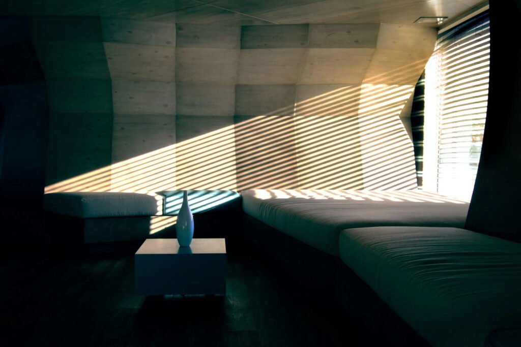 Modern room with sunlight casting stripes on concrete walls and minimalist furniture.