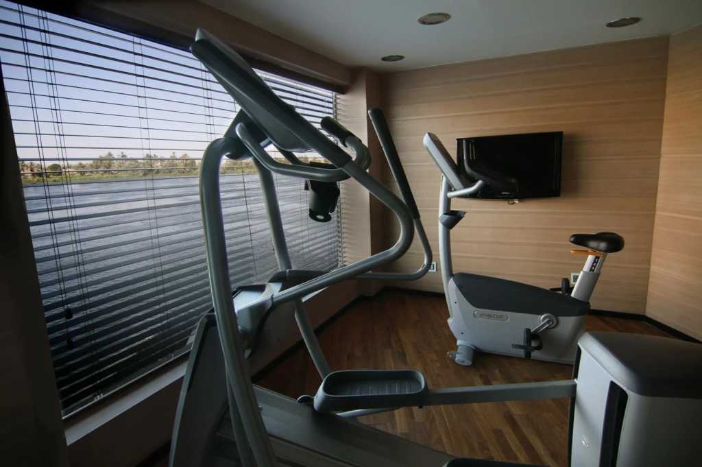 Home gym with an elliptical machine and stationary bike by a window with blinds.