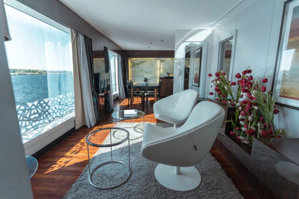 Modern living room with large windows overlooking a lake, white chairs.