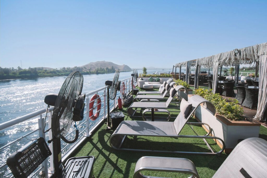 Boat deck with loungers overlooking a river and hills under a clear sky.