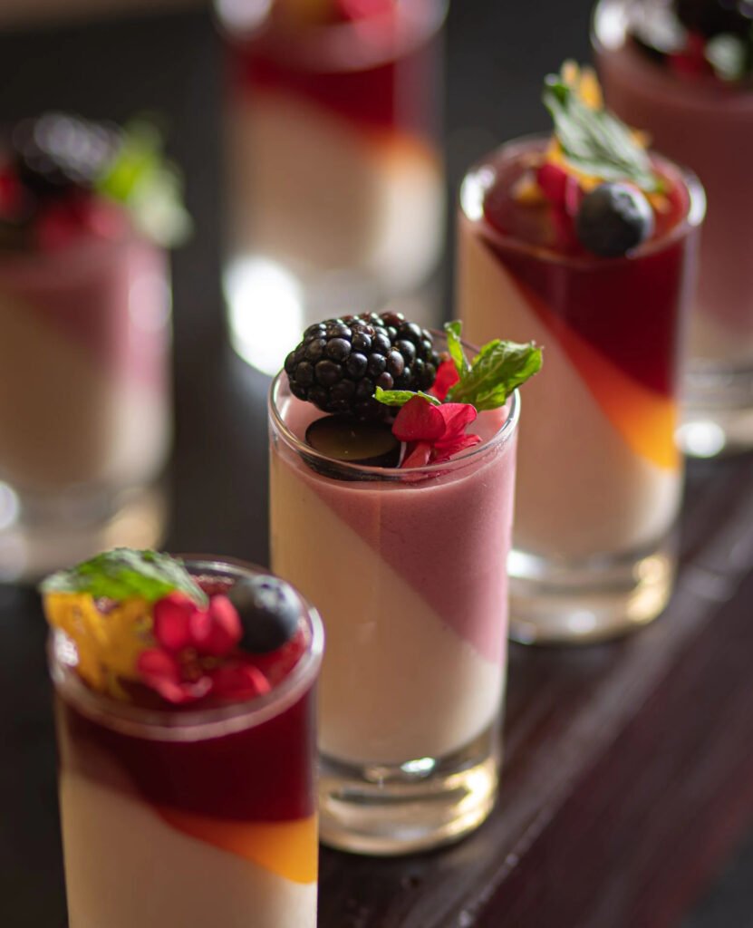 Assorted layered dessert shooters with fruits and mint on top.