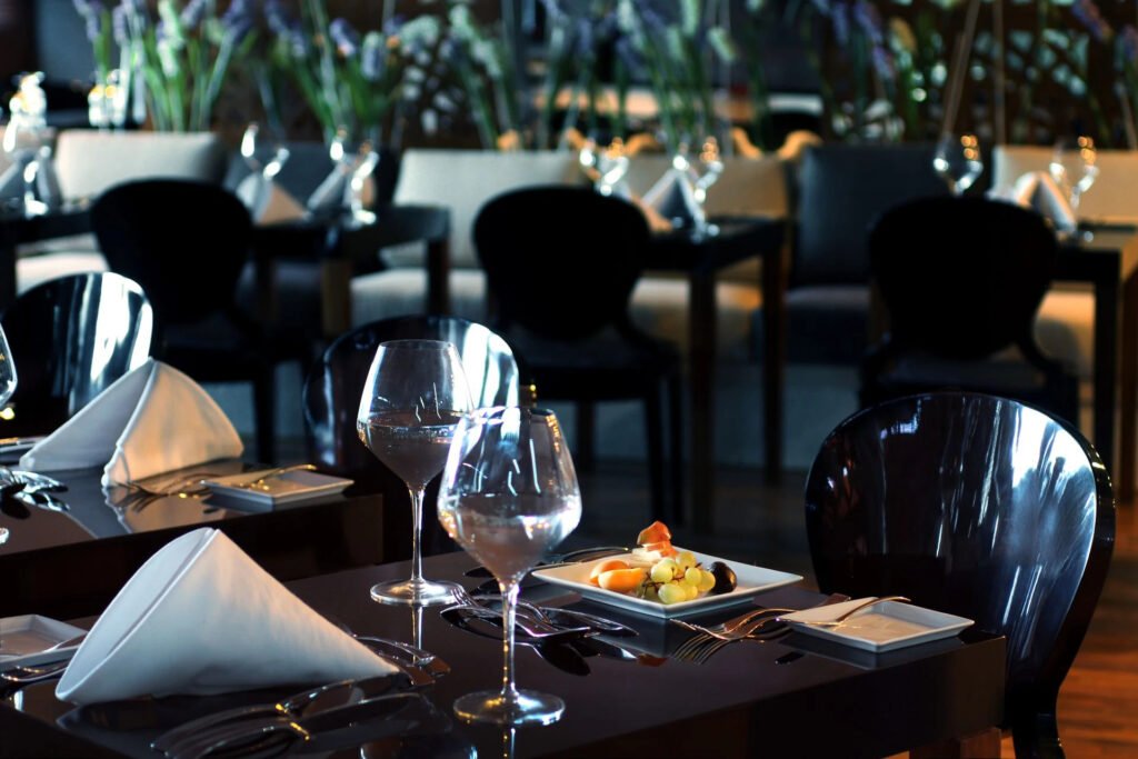 Elegant dining setup with wine glasses, napkins, and a fruit plate in a dimly lit restaurant.