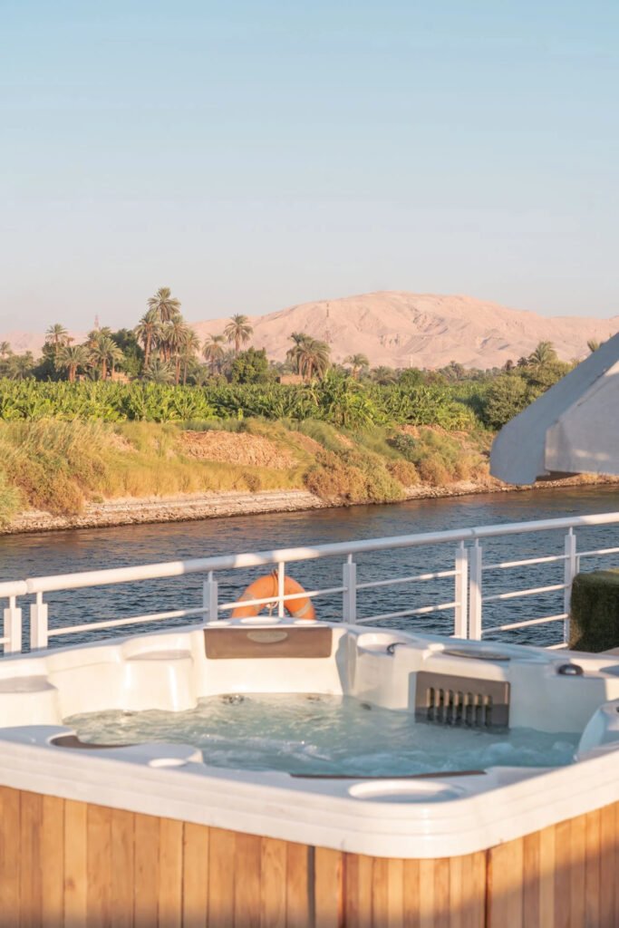 A hot tub on a boat overlooking a river with lush greenery and distant mountains.