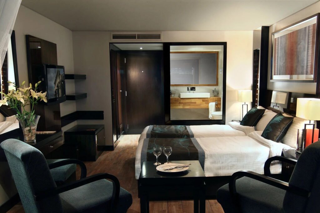 Modern hotel room with a bed, chairs, and view into a bathroom suite.