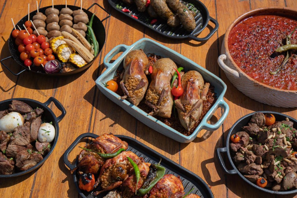 Assorted dishes with grilled meats and vegetables on a wooden table.