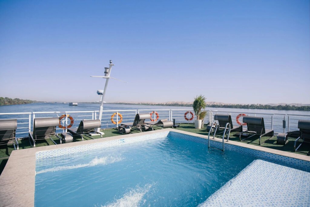 Swimming pool on a cruise deck with sun loungers overlooking a river.