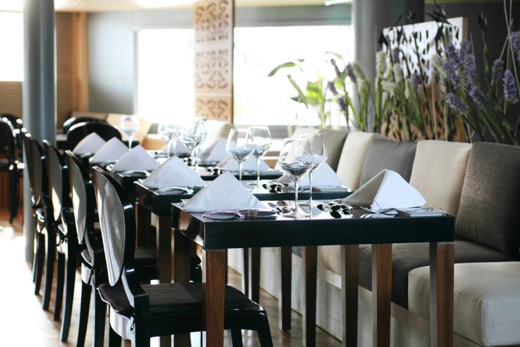 Elegant dining setup with wine glasses, plates, and silverware on sleek tables in a bright restaurant.