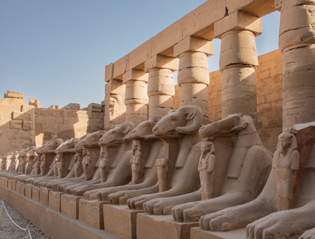 karnak-temple-thebes-luxor-egypt-photograph-2-e28093-one-of-the-two-rows-of-ram-headed-sphinxes-at-the-entrance-to-the-temple-note-that-between-the-forepaws-of-each-sphinx-is-a-statue-of